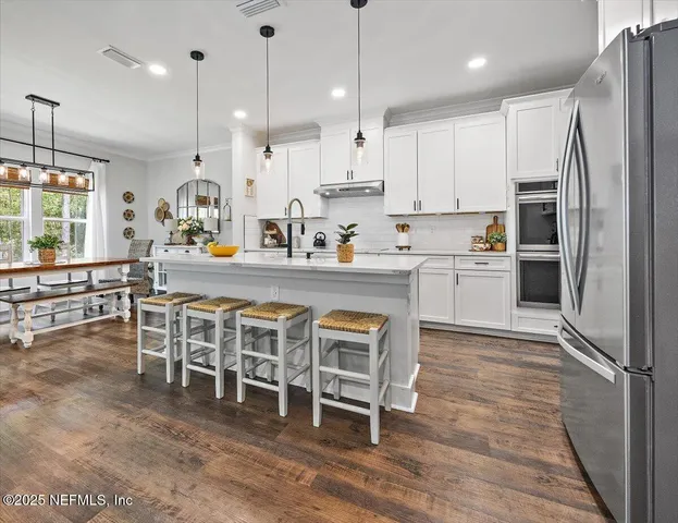 a kitchen with stainless steel appliances granite countertop a table chairs wooden floors a large window and white cabinets