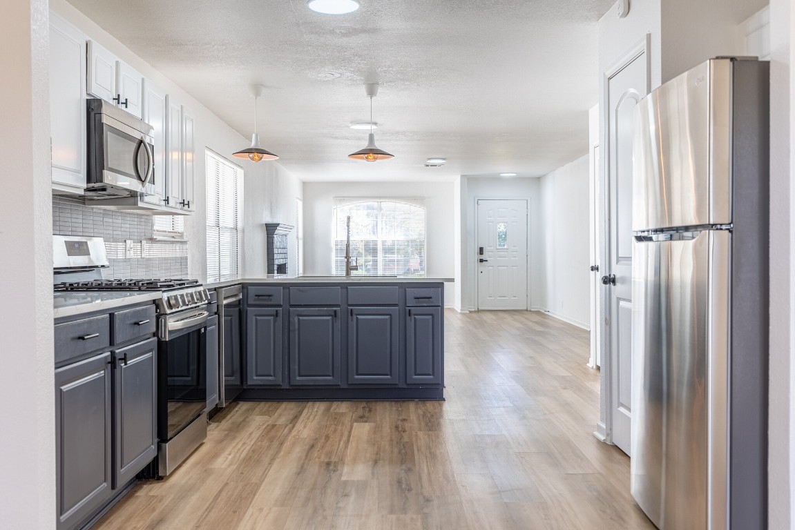 2012 Balsam Way Round Rock, TX 78665 - Photo 11 of 30 Kitchen featuring appliances with stainless steel finishes, a peninsula, light countertops, pendant lighting, and light wood-type flooring