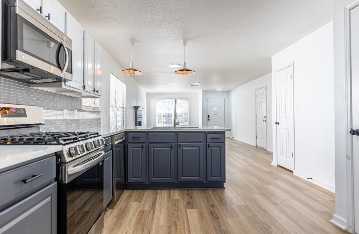 2012 Balsam Way Round Rock, TX 78665 - Photo 10 of 30 Kitchen featuring stainless steel appliances, a peninsula, tasteful backsplash, light wood-type flooring, and decorative light fixtures