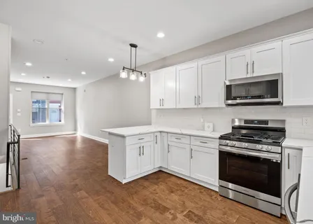 a kitchen with stainless steel appliances granite countertop a refrigerator a stove and white cabinets with wooden floors