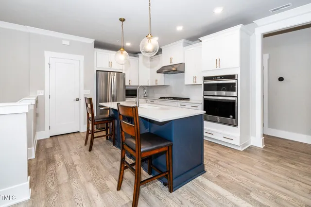 a kitchen with stainless steel appliances a stove a refrigerator a kitchen island a sink cabinets and wooden floor