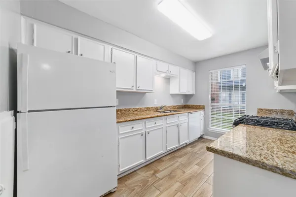 a kitchen with granite countertop a refrigerator a sink a stove and white cabinets