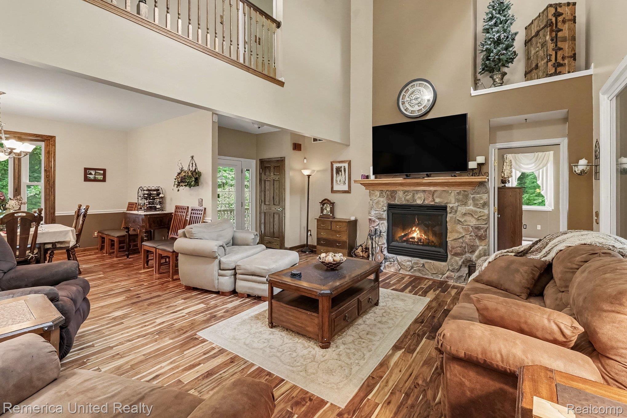 20962 Wasson Road Gregory, MI 48137 - Photo 4 of 39 Two-story living area featuring a stone-clad fireplace with a wood mantel, high ceilings, wood-finish flooring, and a second-story overlook with a wood railing
