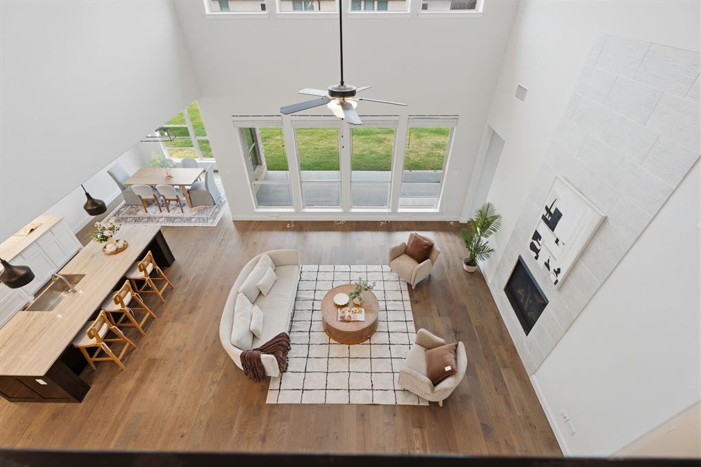 1316 Limestone Ridge Road Mansfield, TX 76063 - Photo 29 of 40 Expansive open-concept living area featuring high ceilings, wood-finish flooring, a contemporary fireplace with floor-to-ceiling tile surround, and large windows offering abundant natural light