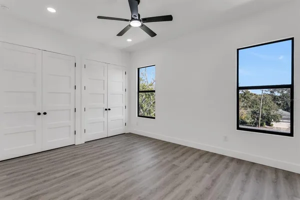 an empty room with wooden floor chandelier fan and windows