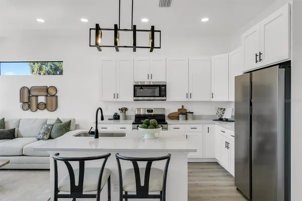 a kitchen with stainless steel appliances kitchen island granite countertop a refrigerator a stove a sink and white cabinets with wooden floor