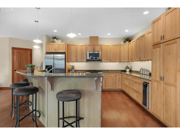 a kitchen with stainless steel appliances granite countertop a stove a sink a refrigerator and a dining table with wooden floor