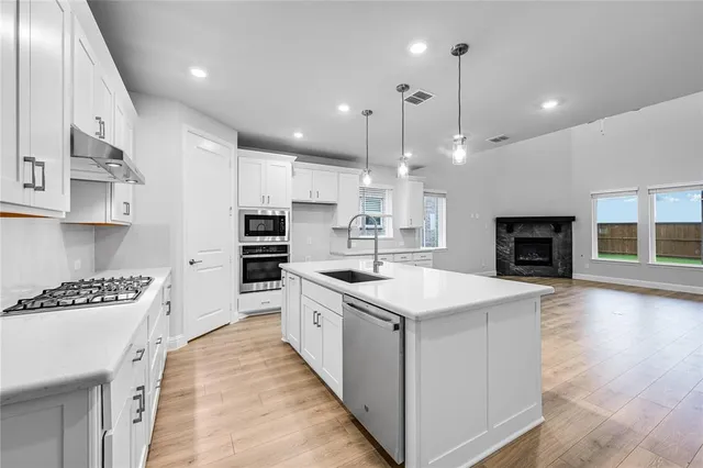 a kitchen with stainless steel appliances kitchen island a large stove a sink dishwasher and a refrigerator with wooden floor