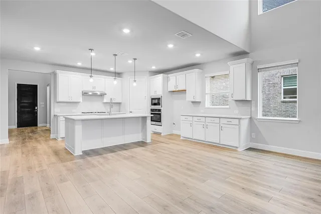 a large white kitchen with kitchen island a sink wooden floor and a refrigerator