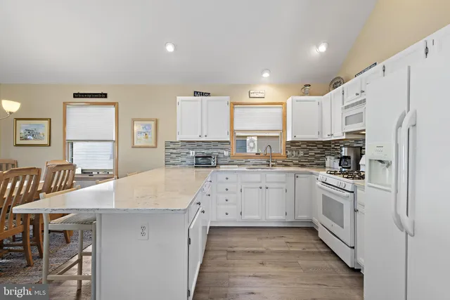 a large kitchen with kitchen island a stove a sink a refrigerator and white cabinets with wooden floor