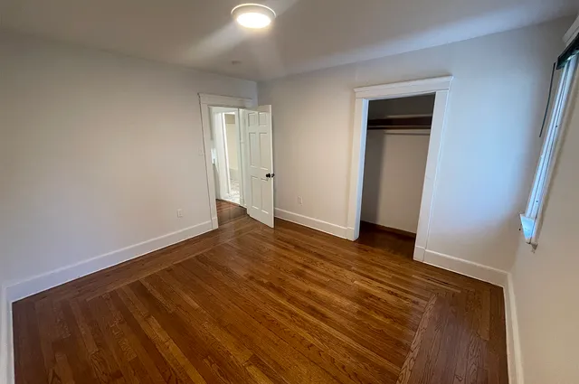 a view of an empty room with wooden floor and closet