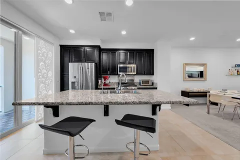 a large kitchen with granite countertop a counter space chairs stainless steel appliances and cabinets