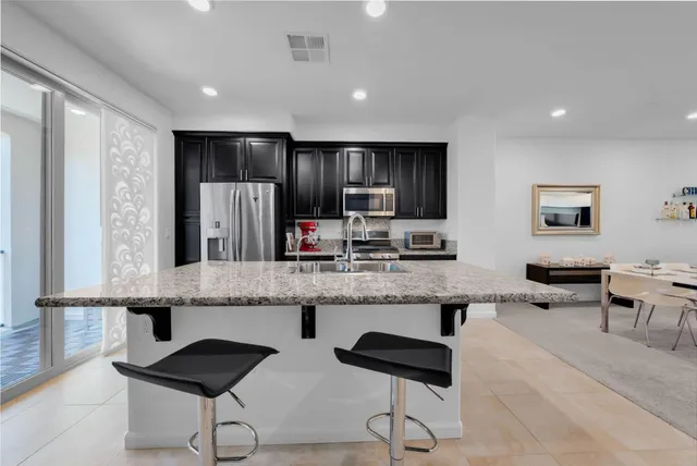 a large kitchen with granite countertop a counter space chairs stainless steel appliances and cabinets