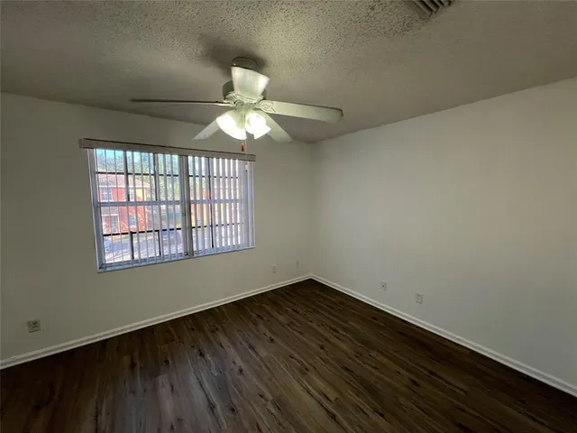 an empty room with wooden floor fan and windows