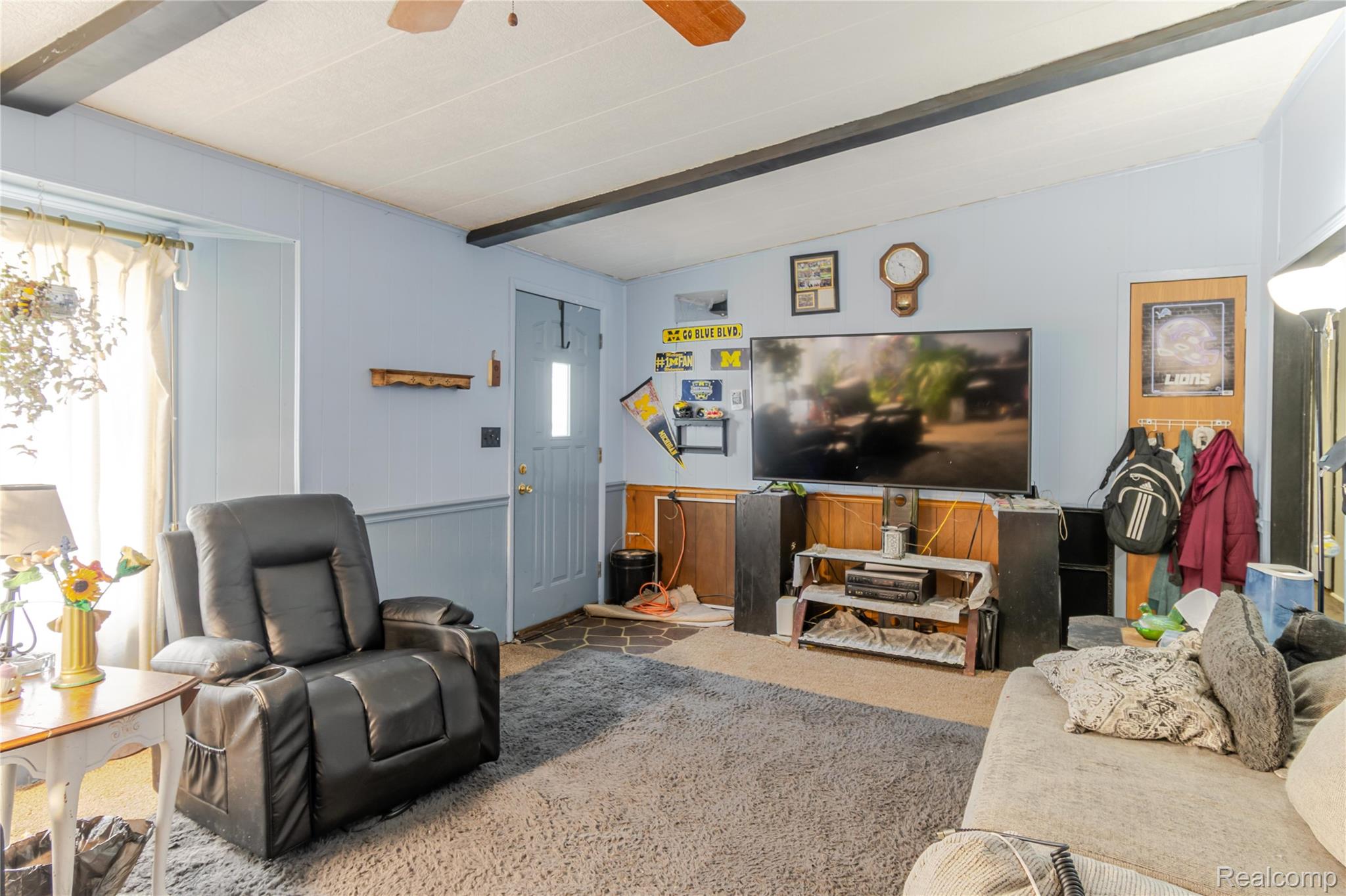 6655 Jackson Road, Unit 126 Ann Arbor, MI 48103 - Photo 10 of 36 Carpeted living area featuring beamed ceiling, wood walls, a ceiling fan, wainscoting, and a decorative wall
