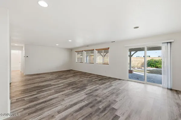a view of an empty room with wooden floor and a kitchen