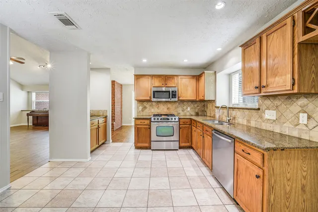 a large kitchen with stainless steel appliances granite countertop a stove top oven a sink dishwasher and a refrigerator with wooden floor