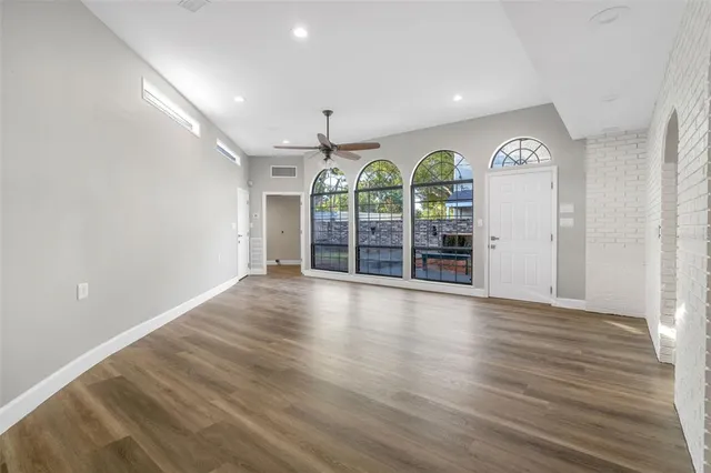 an empty room with wooden floor fan and windows