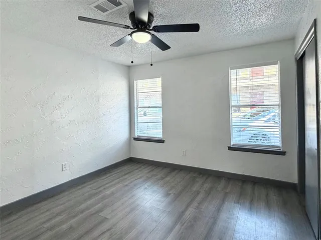 an empty room with wooden floor chandelier fan and windows