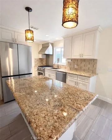 a kitchen with kitchen island granite countertop a refrigerator a stove and a sink with granite countertops