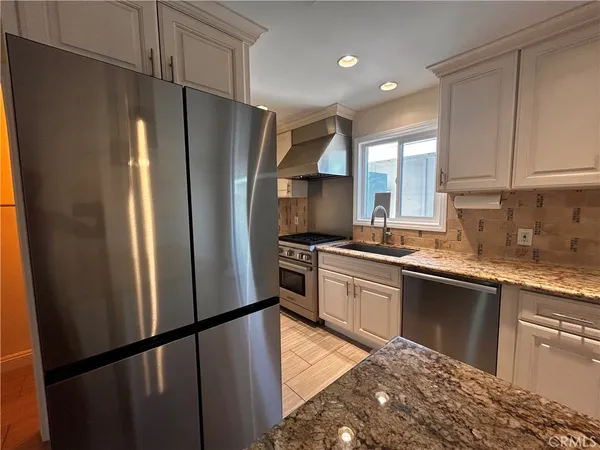 a kitchen with stainless steel appliances granite countertop a refrigerator a sink dishwasher a stove and white cabinets with wooden floor