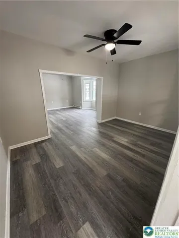 a view of an empty room with wooden floor and a ceiling fan