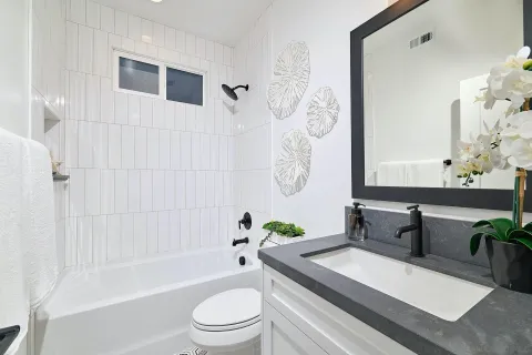 a bathroom with a granite countertop sink a toilet a mirror a bathtub and shower