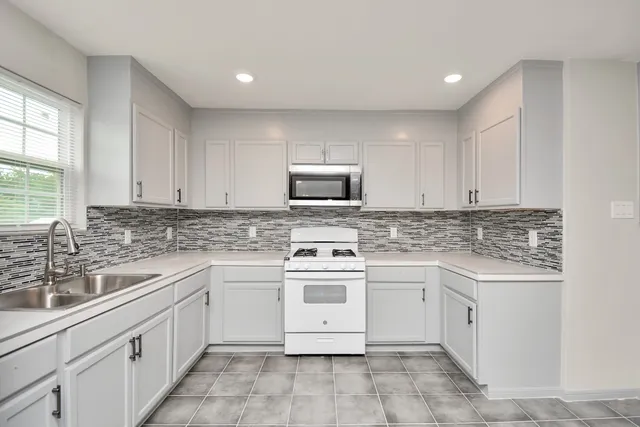 a kitchen with white cabinets appliances a sink and a window