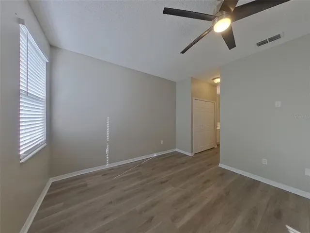 an empty room with wooden floor ceiling fan and windows