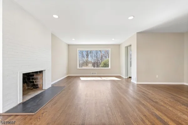 an empty room with wooden floor fireplace and windows