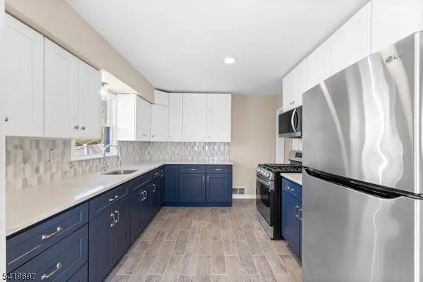 a kitchen with stainless steel appliances granite countertop a refrigerator a sink dishwasher a stove and white countertops with wooden floor