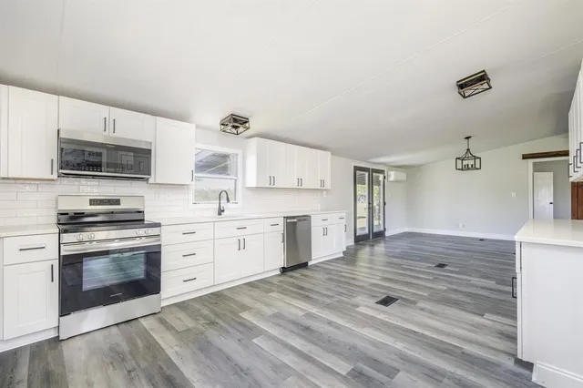 a kitchen with stainless steel appliances granite countertop a stove top oven a sink dishwasher and a refrigerator with white cabinets