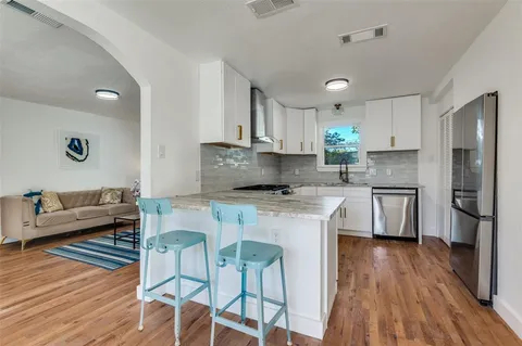 a kitchen with stainless steel appliances white cabinets a sink a stove a refrigerator and wooden floor