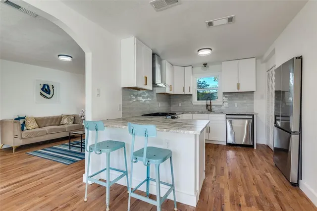 a kitchen with stainless steel appliances white cabinets a sink a stove a refrigerator and wooden floor