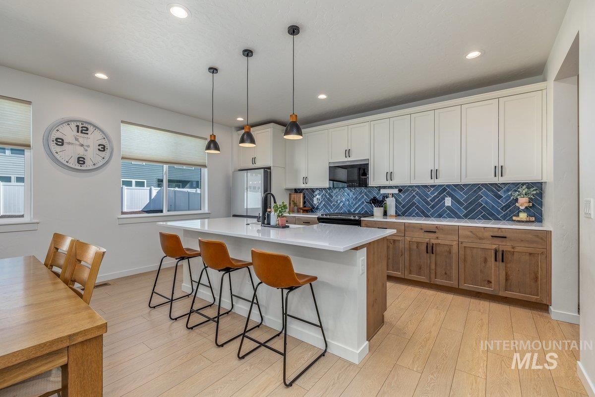 1380 West Chilitna Street Meridian, ID 83642 - Photo 6 of 50 Bright kitchen featuring a substantial island with countertop seating, white shaker-style upper cabinetry, wood-finish lower cabinetry, and a blue herringbone tile backsplash