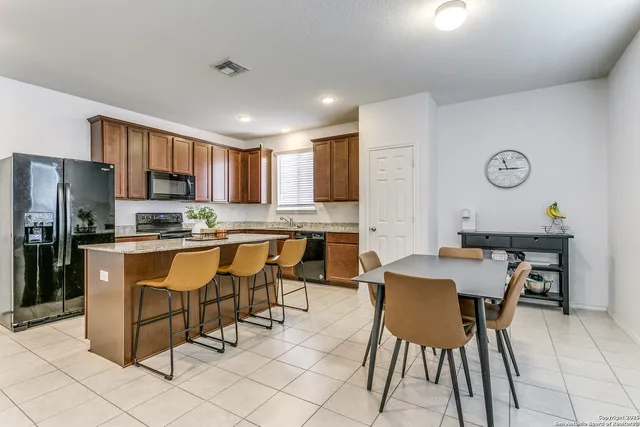 a kitchen with stainless steel appliances granite countertop a stove a sink a microwave a refrigerator and chairs