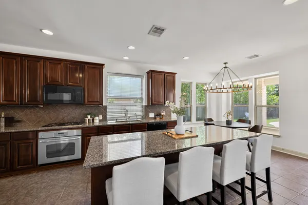 a kitchen with stainless steel appliances granite countertop a stove a sink dishwasher a microwave oven and a dining table with wooden cabinet