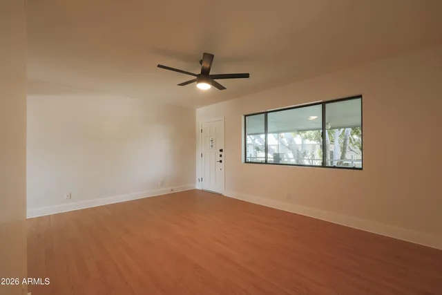 an empty room with wooden floor fan and windows