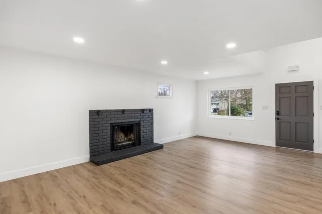 a view of an empty room with wooden floor fireplace and a window
