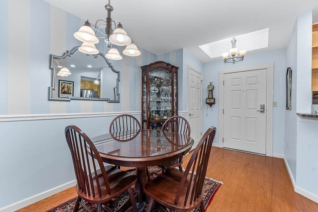 989 East Street, Unit 402 Dedham, MA 02026 - Photo 6 of 28 a dining room with wooden floor a chandelier a wooden table and chairs