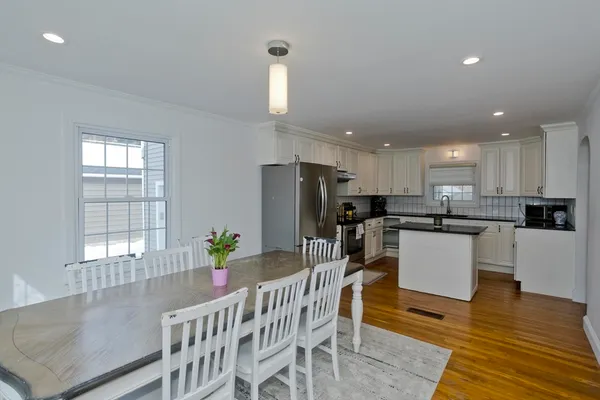 a kitchen with stainless steel appliances kitchen island granite countertop a refrigerator a stove a sink dishwasher and a dining table with wooden floor