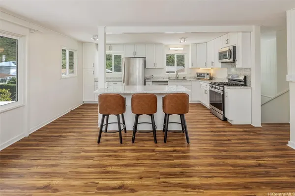 a kitchen with stainless steel appliances granite countertop a stove top oven a sink dishwasher and a refrigerator with wooden floor