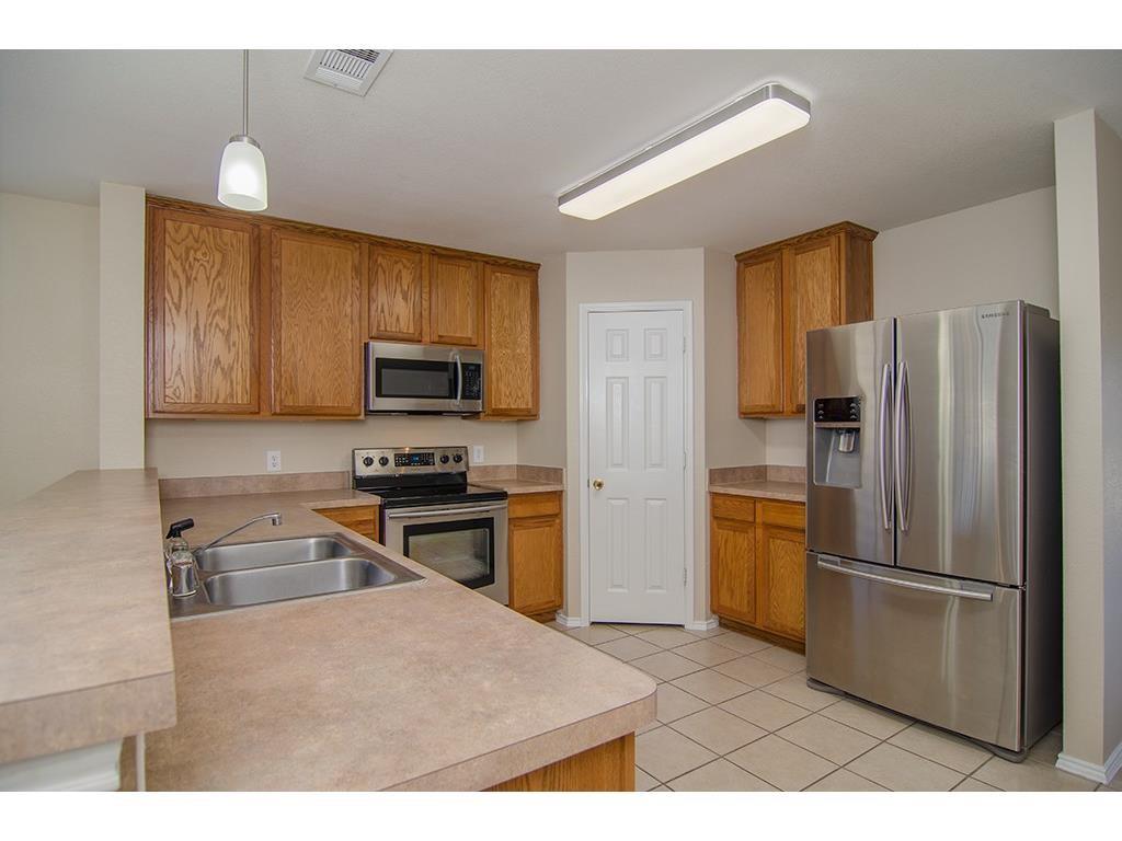 13109 Fieldstone Road Fort Worth, TX 76244 - Photo 11 of 25 Kitchen with stainless steel appliances, wood finish cabinetry, a peninsula, pendant lighting, and light tile patterned floors