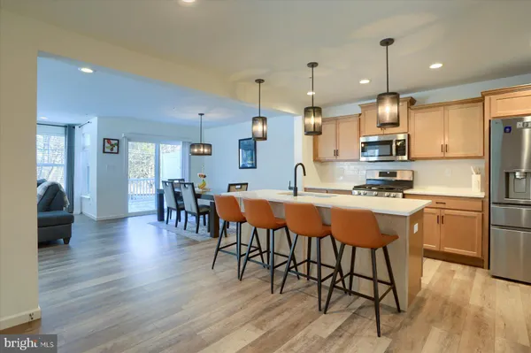 a kitchen with stainless steel appliances granite countertop a stove a refrigerator a kitchen island a dining table and chairs with wooden floor