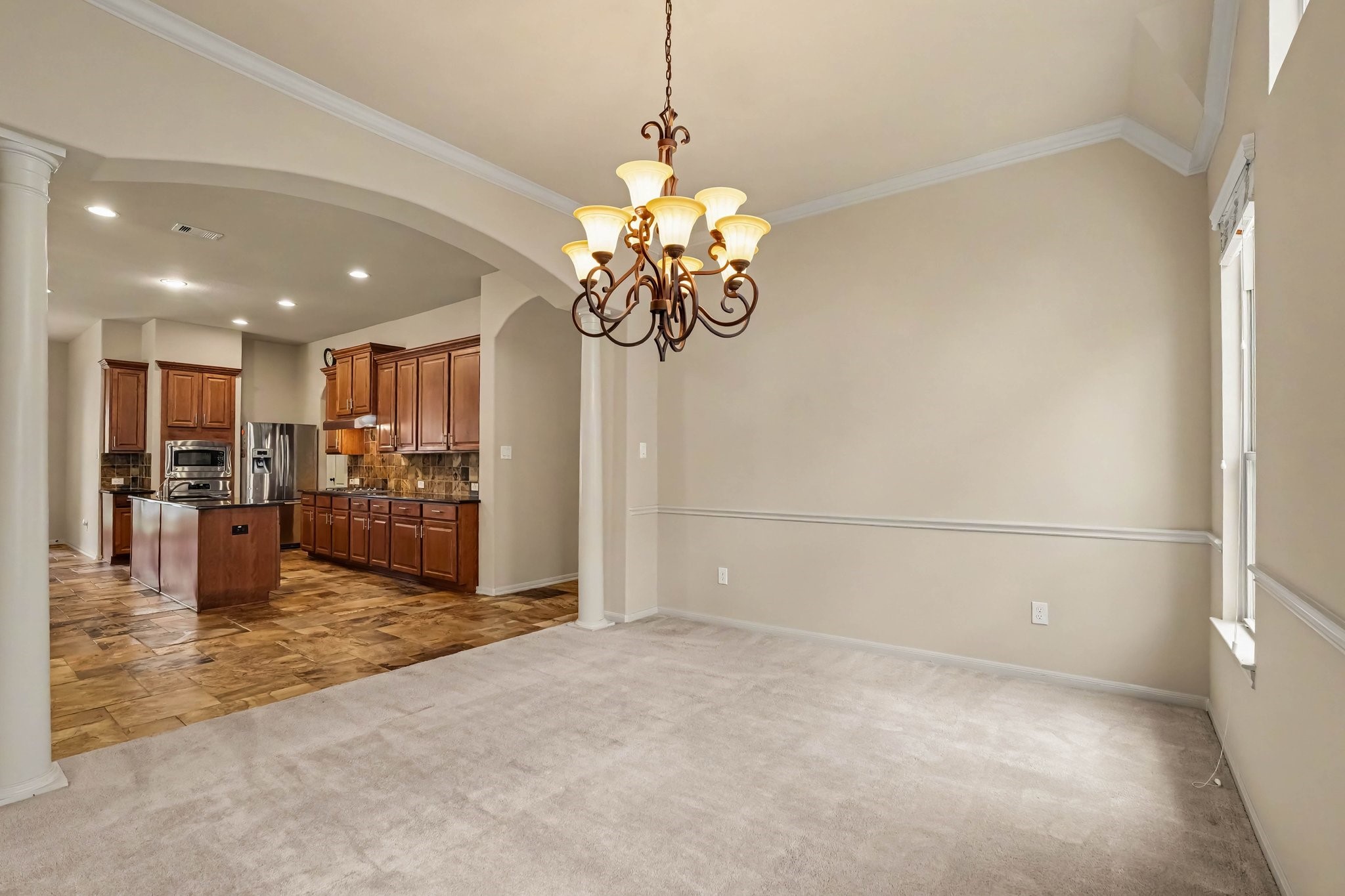 62 Sandwell Place Spring, TX 77389 - Photo 15 of 50 Elegant dining area with a stylish chandelier and soft carpeting, leading into a spacious kitchen featuring rich wood cabinetry, modern appliances, and a central island.