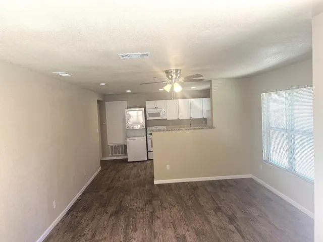 an empty room with wooden floor and kitchen view
