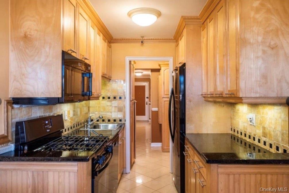 450 Pelham Road, Unit 3B New Rochelle, NY 10805 - Photo 12 of 22 Kitchen with black appliances, tasteful backsplash, light tile patterned floors, ornamental molding, and dark stone countertops