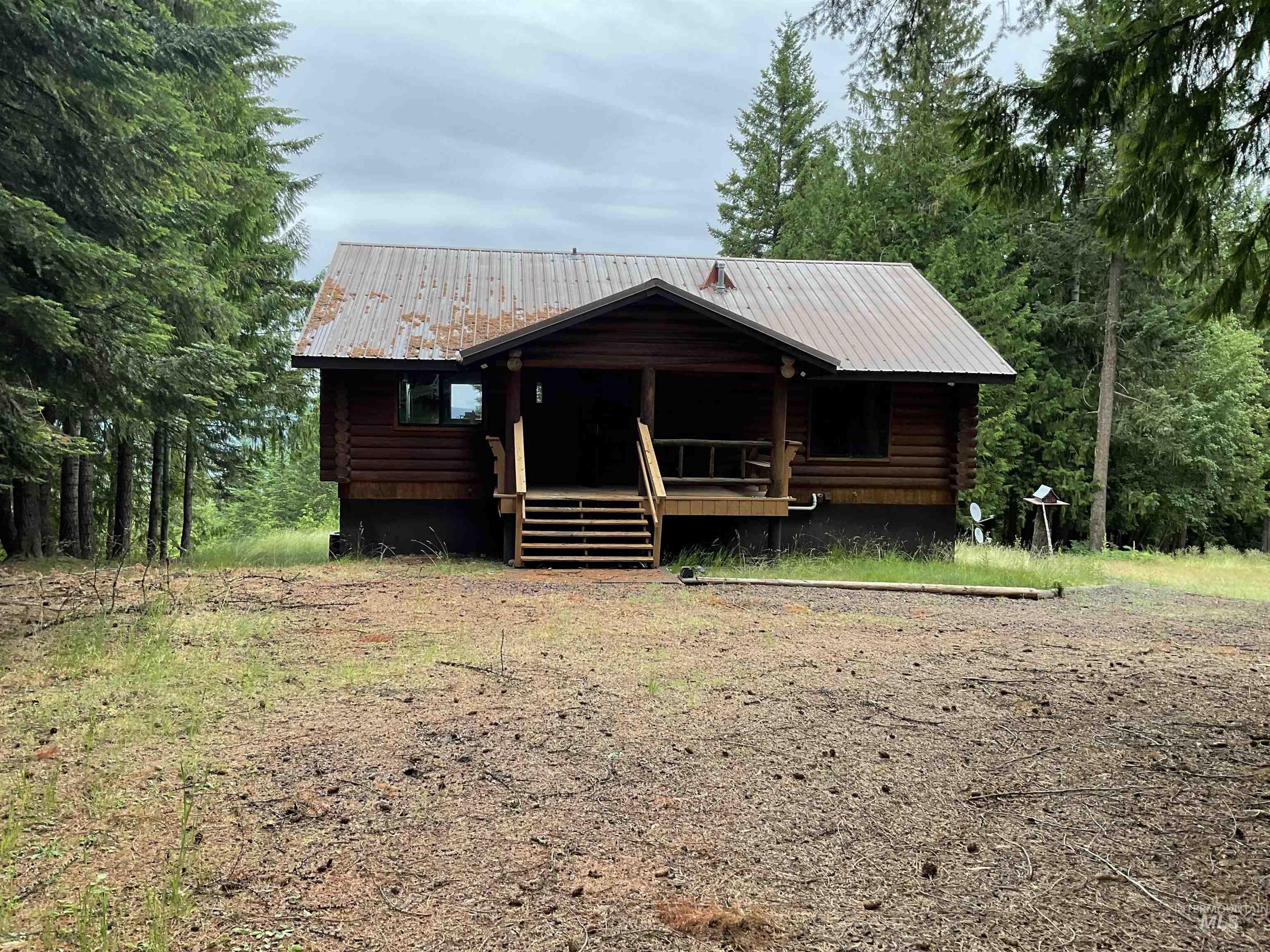 6125 Freeman Creek Road Lenore, ID 83541 - Photo 4 of 44 Log cabin exterior featuring a covered front porch with wood railings and steps, a metal roof, and surrounding mature evergreen trees