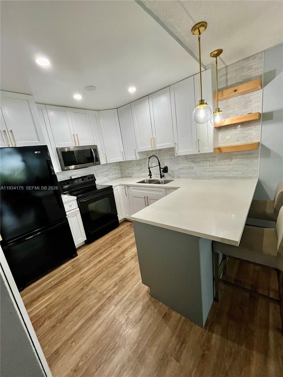 1750 West 56th Street, Unit 211 Hialeah, FL 33012 - Photo 3 of 19 a kitchen with a sink dishwasher a stove a microwave oven and a dining table with wooden floor