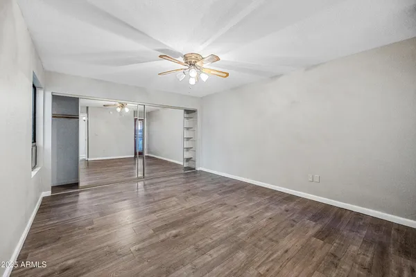 an empty room with wooden floor fan and windows